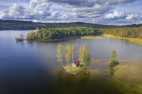 Aerial view over small traditional red wooden cabin on tiny island in lake in autumn, fall,