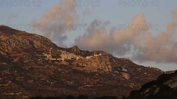 A village on a rocky plateau in a mountain range at sunrise under a cloudy sky, mountain village