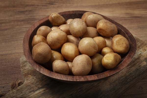 A wooden bowl filled with fresh small potatoes is centered on a rustic wooden table, showcasing