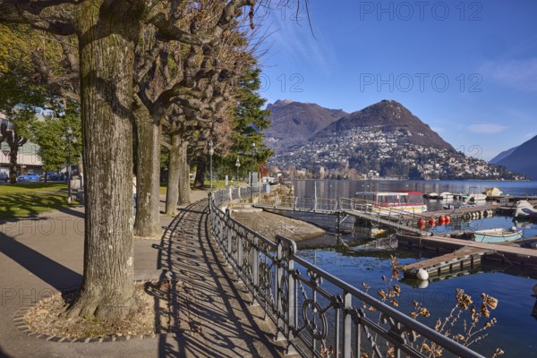 Lakeside promenade, railing with shade, trees, lake, mountains, blue sky, Lake Lugano, Lugano,