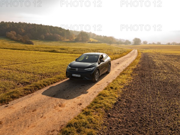 A car drives along a remote country lane through an autumn landscape full of fields, electric car