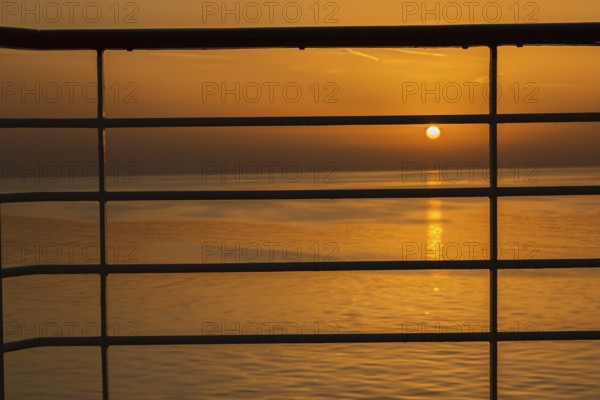 Close-up of silhouetted railing on cruise ship and golden setting sun over Adriatic sea near Zadar,