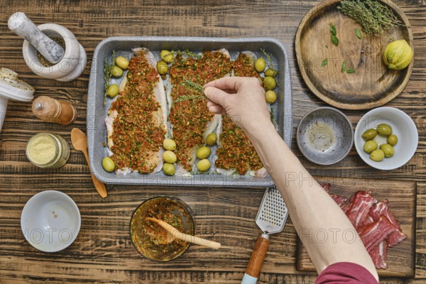 A person adding thyme to fish fillets with a vibrant herb mixture, surrounded by fresh ingredients