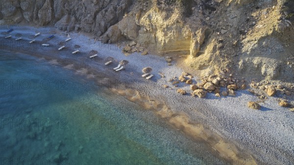 Pebble beach with clear blue waves and rocky coastline. Silence and seclusion, beach loungers,