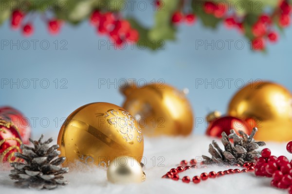 Golden and red Christmas baubles lie on artificial snow, surrounded by cones and red berries