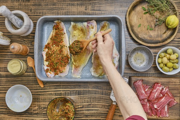 Fish fillets are laid out in a tray, being generously coated with a mix of herbs and spices.