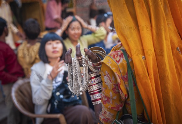 Woman in traditional Rajasthani dress selling jewellery to Japanese tourists, old town of Pushkar