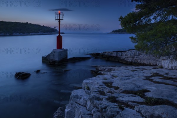 Lighthouse or red sea mark on a rocky coast at dusk, surrounded by gentle waves, Hvar, Dalmatia,