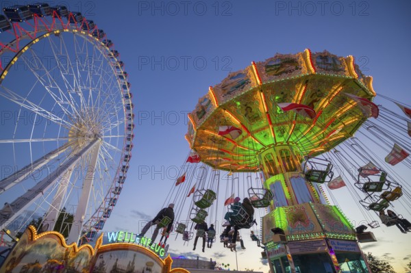 A funfair at dusk with illuminated chain carousel and Ferris wheel, Europa Rad, rides, wave flight,