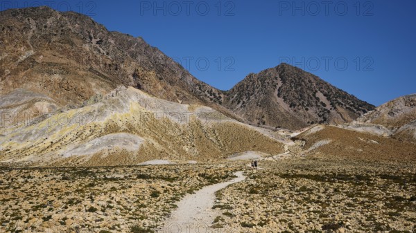 Hiking trail leading through a barren mountain landscape under a bright blue sky, volcanism,
