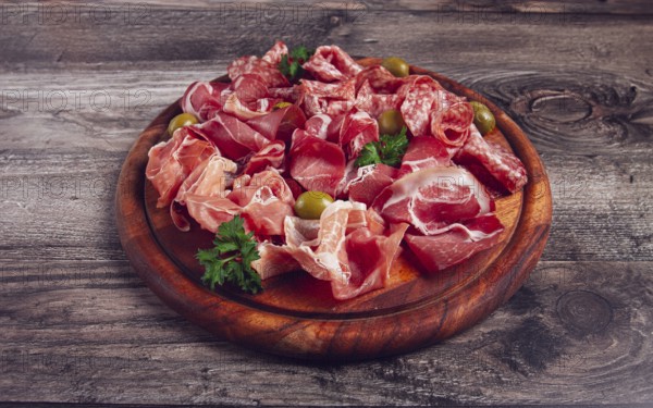 Assortment, sliced meat appetizer, prosciutto, salami and ham, with olives, on a wooden board,