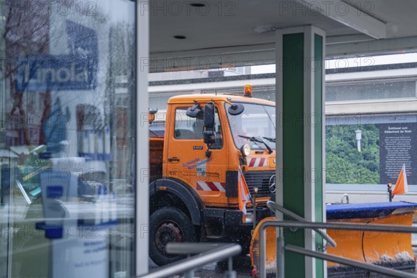 Orange snow clearing vehicle in front of a shop window in a wintry environment, Sindelfingen,