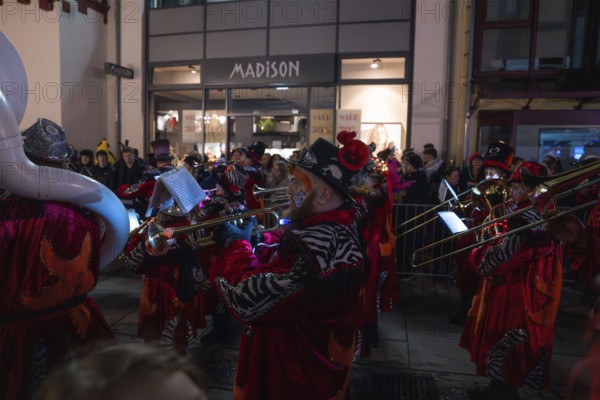 A band playing music in colourful costumes performs at night on a busy street, carnival, Calw,