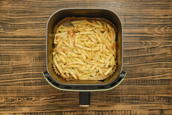 Freshly cooked golden french fries are in an air fryer, showcasing their crispy texture