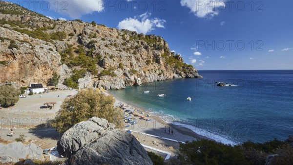 Sweeping view over a bay with rocks, blue sea and beachgoers on a sunny day, Ahata Beach, Ahata,