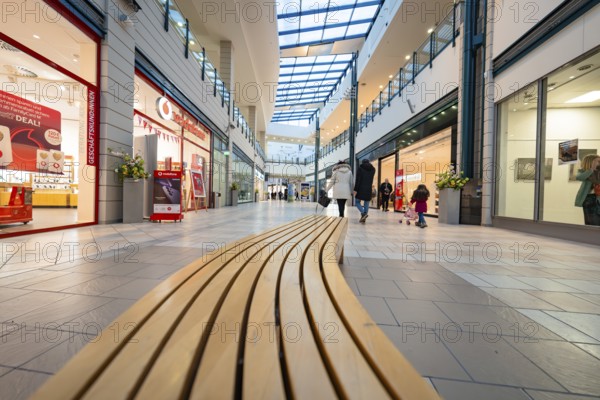 Interior view of a shopping centre with long wooden bench and glass roof, family atmosphere,