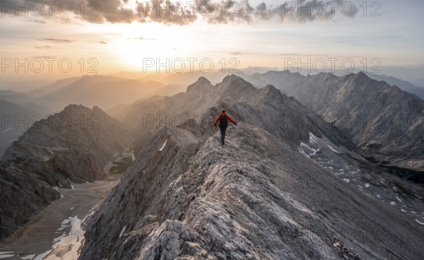 Mountaineer with helmet on a narrow rocky ridge at sunrise, crossing the Jubiläumsgrat, view of