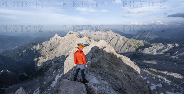Mountaineer on a narrow rocky steep ridge, view of the Höllental and the Alpspitze from the