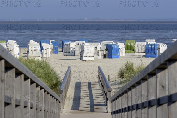 View from a wooden plank path to the beach with beach chairs, the island of Juist on the horizon,