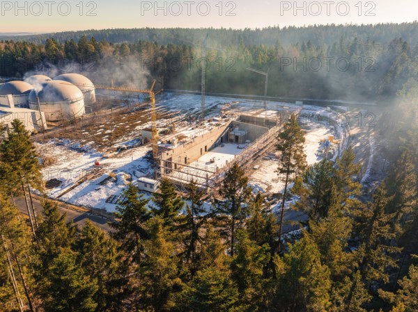 Snow-covered construction site next to domed buildings in the forest, with construction crane, new