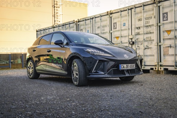 Black car with company logo in an industrial estate in front of containers, Deer E- Carsharing