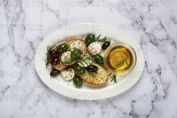 A plate with a snack, ciabatta bread with cheese and olives, olive oil, spices and herbs, top view,