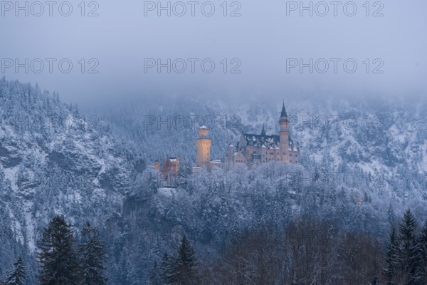 Castle rises above a quiet, snow-covered winter landscape under a misty sky, illuminated,