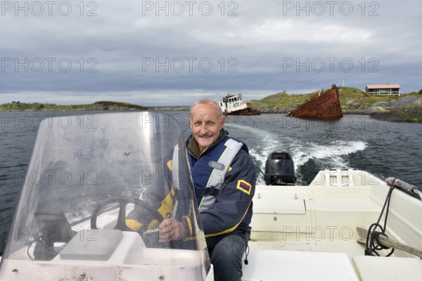 Man, senior driving motorboat, fishing boat at a shipwreck on the Atlantic Road in Norway