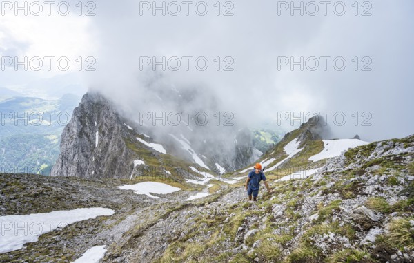 Mountaineer with helmet on a narrow hiking trail, ascent to the Ackerlspitze, clouds moving around