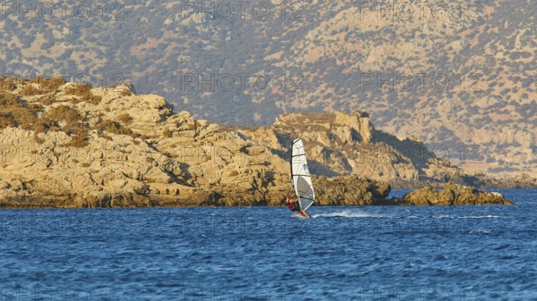 A windsurfer rides near the rocky coast in calm weather, windsurfer, Meltemi windsurfing spot,