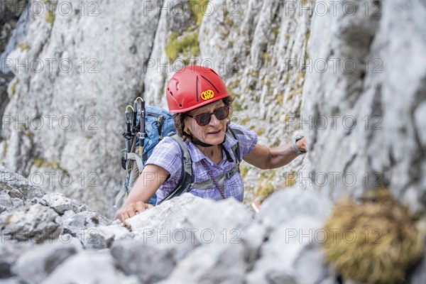 Female mountaineer with helmet climbing a rock face, ascent to the Ackerlspitze, Wilder Kaiser,