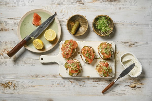 Salmon toasts topped with fresh watercress sprouts on a white cutting board. Slices of lemon and