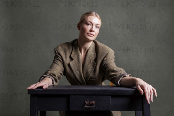 Woman sitting seriously at a dark table in front of a green background in smart clothes, photo