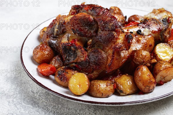 Pork knuckle baked with vegetables, new potatoes, on a white plate, homemade, no people