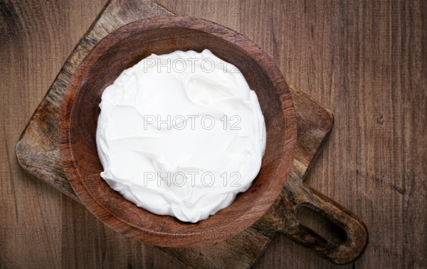 Sour cream in a wooden bowl, on a wooden table, top view, close-up, no people