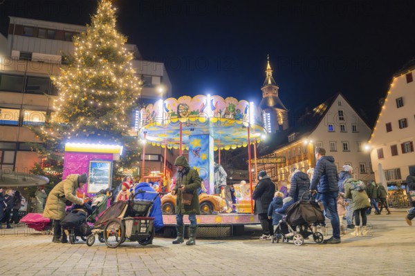 Christmas market at night with illuminated carousel and Christmas tree, surrounded by people and a