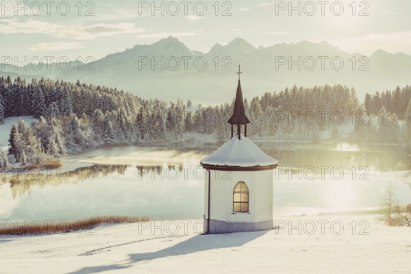 Chapel by the lake in the wintry snow-covered Allgäu near Halblech in front of an impressive