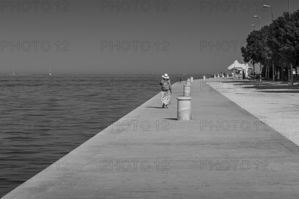 Lonely walker on a long pedestrian path along the coast in black and white, Zadar, Croatia, Europe