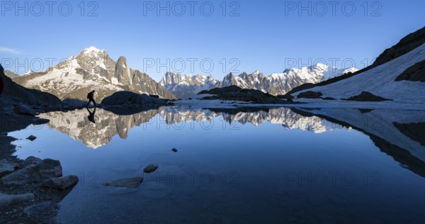 Mountaineer, silhouette in front of mountain landscape in the evening light, water reflection in