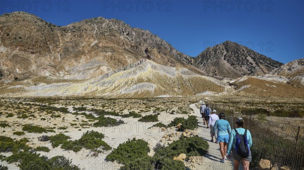People walking on a path through a mountainous landscape under a clear sky, volcanism, volcanic
