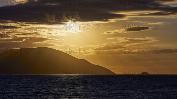 The sky shows a dramatic sunset with dark clouds and an island on the horizon, sunset, Kassos,
