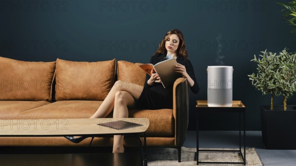 Young well dressed woman sits on couch in lobby near air purifier and reading magazine