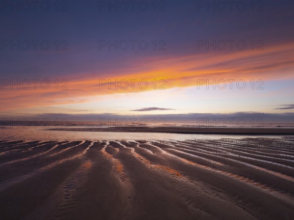 Evening sky after sunset, over the coastline at low tide, showing the ribbed sand formations and