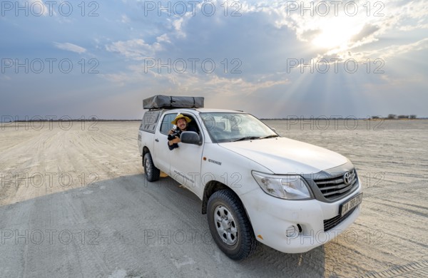 Young man with camera looking out the window of an off-road vehicle, Toyota Hilux on a salt pan,