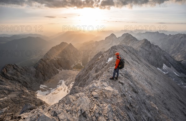 Mountaineer with helmet on a narrow rocky ridge at sunrise, crossing the Jubiläumsgrat, view of