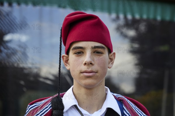 Young man in traditional Cretan dress with red hat, serious expression, visit of the Federal