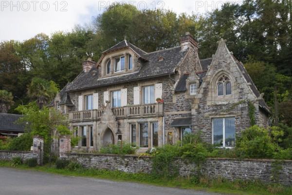 Historic stone house surrounded by trees with elaborate details and large windows,