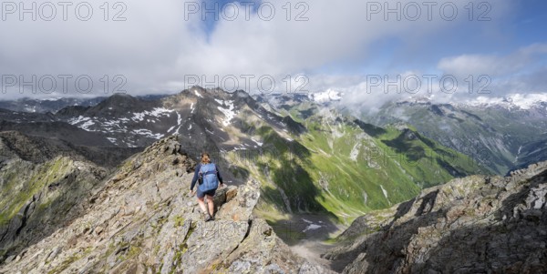 Mountaineer on a steep rocky ridge, on the summit of the Lasörling, view of the mountain panorama