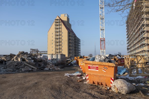 Construction site with high-rise building and crane, surrounded by piles of rubble, old warehouse