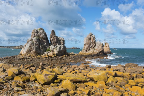 Rocky coast with stormy waves under a blue sky with white clouds, Plage de Pors Scaff,